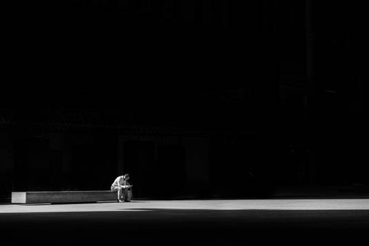 a person sitting with their head down on a black background