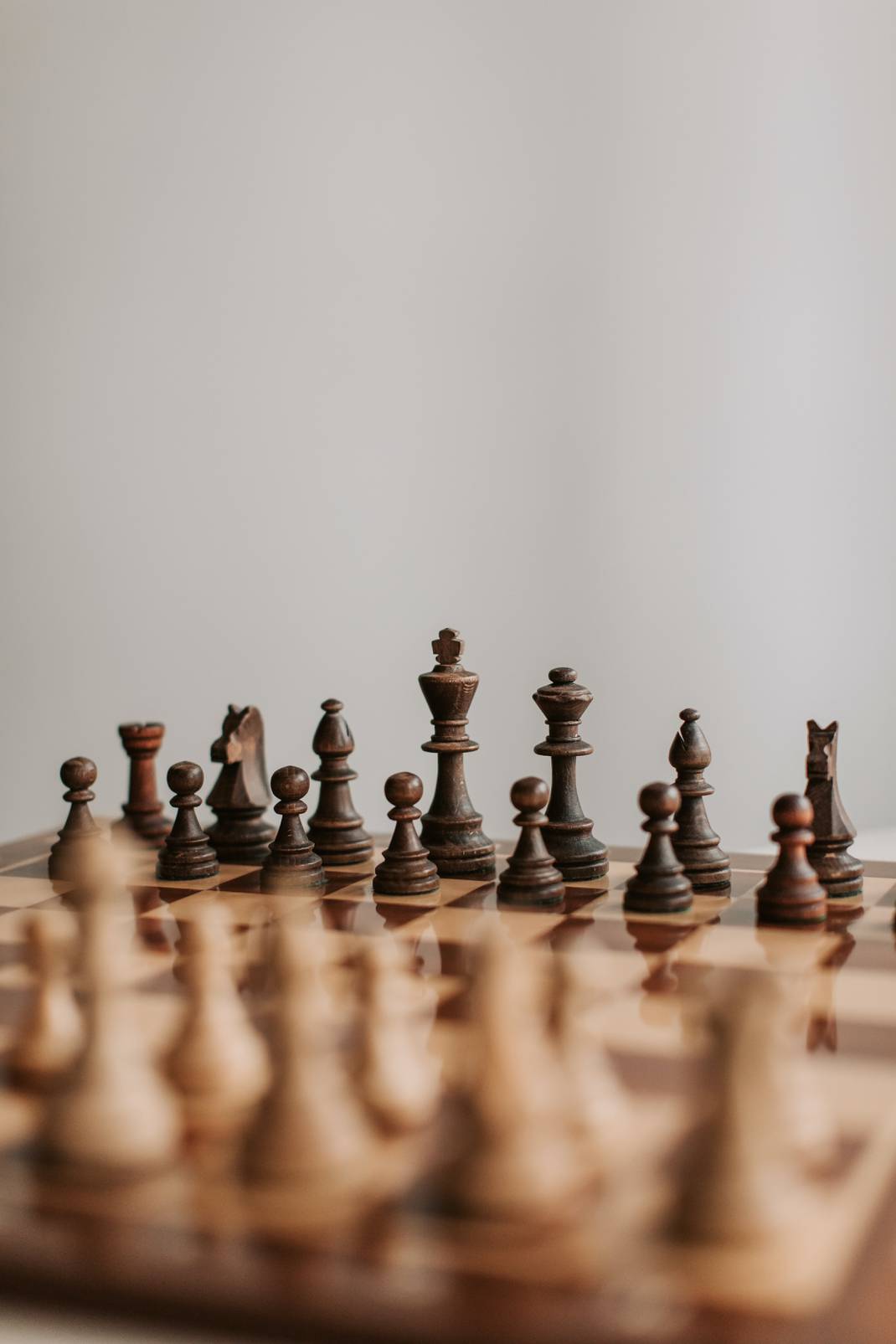 A chess board with the white pieces close and faded and the black pieces in focus.