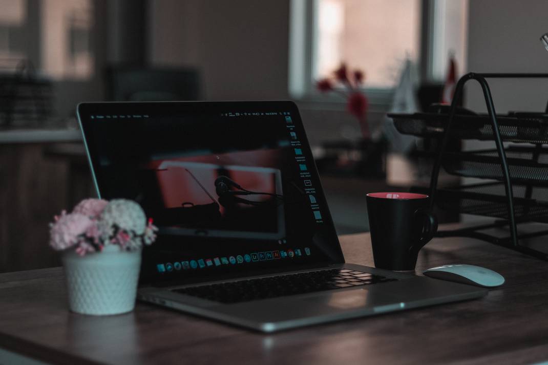 A photo of a computer with a vase with flowers and a coffee mug on each side